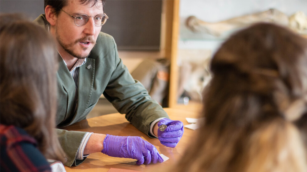 A lecturer talks to students while handling an artefact